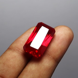 Puede incluir: Una piedra preciosa de color rojo intenso con un corte rectangular esmeralda.