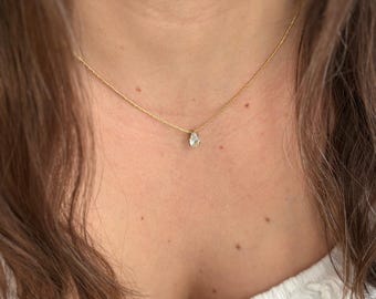 May include: A delicate gold chain necklace with a single pear-shaped clear gemstone pendant.