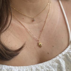 Puede incluir: Dos collares de oro con colgantes. El collar superior tiene un pequeño colgante de piedra preciosa transparente. El collar inferior tiene un colgante en forma de estrella.
