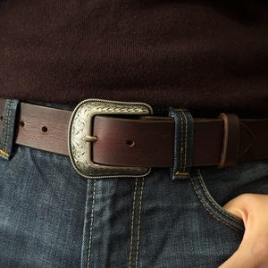 Puede incluir: Un cintur&oacute;n de cuero marr&oacute;n con una hebilla plateada decorativa. El cintur&oacute;n se usa con vaqueros azules y un su&eacute;ter marr&oacute;n oscuro. La hebilla tiene un dise&ntilde;o ornamentado. El cintur&oacute;n mide aproximadamente 3,8 cm de ancho.