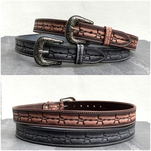 Op de afbeelding: Twee leren riemen met zilverkleurige gespen. E&eacute;n riem is bruin met een prikkeldraadontwerp, de andere is zwart met een vergelijkbaar patroon. Beide hebben witte stiksels. Geschikt voor taillematen van 76 cm tot 102 cm.