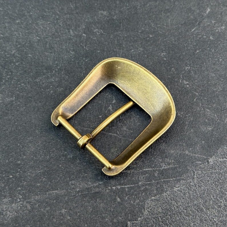 Puede incluir: Hebilla de cintur&oacute;n de lat&oacute;n de estilo vintage con un marco rectangular y una parte superior curvada. La hebilla tiene un dise&ntilde;o cl&aacute;sico con un pasador para asegurar el cintur&oacute;n. El metal tiene un aspecto ligeramente envejecido.