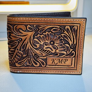 May include: A brown leather wallet with a floral tooled design and the initials "KMP" embossed on the front.