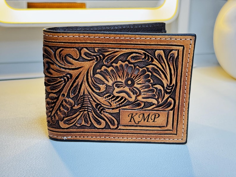 May include: A brown leather wallet with a floral tooled design and the initials "KMP" embossed on the front.