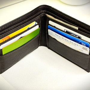 May include: A brown leather wallet with multiple card slots, open to reveal several cards, including a New York State Identification Card.