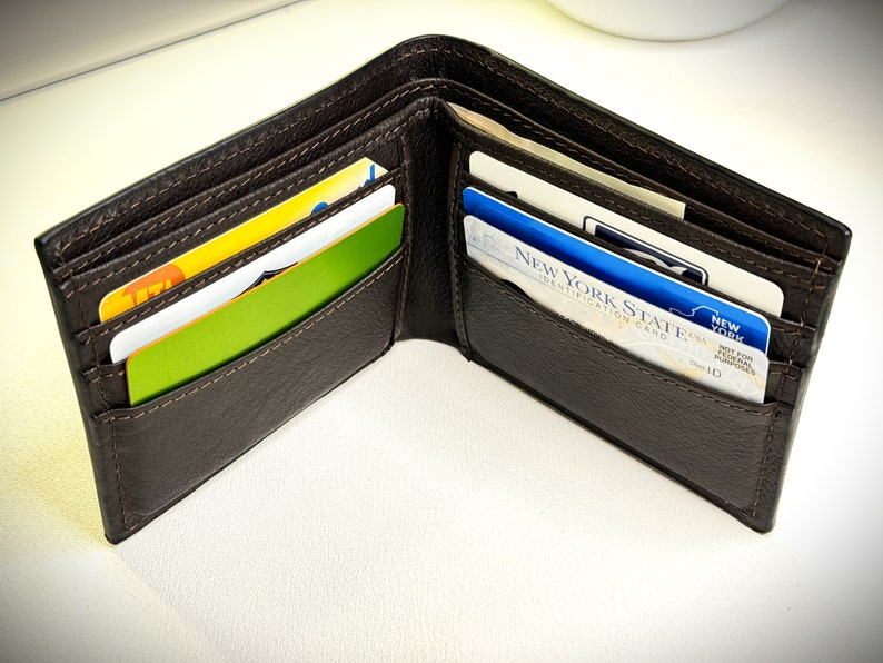 May include: A brown leather wallet with multiple card slots, open to reveal several cards, including a New York State Identification Card.