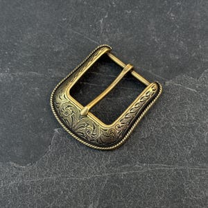 Puede incluir: Hebilla de cintur&oacute;n de lat&oacute;n de estilo antiguo con intrincados grabados florales y de volutas. La hebilla rectangular presenta un dise&ntilde;o de cuerda en los bordes. La hebilla tiene una est&eacute;tica cl&aacute;sica y occidental.