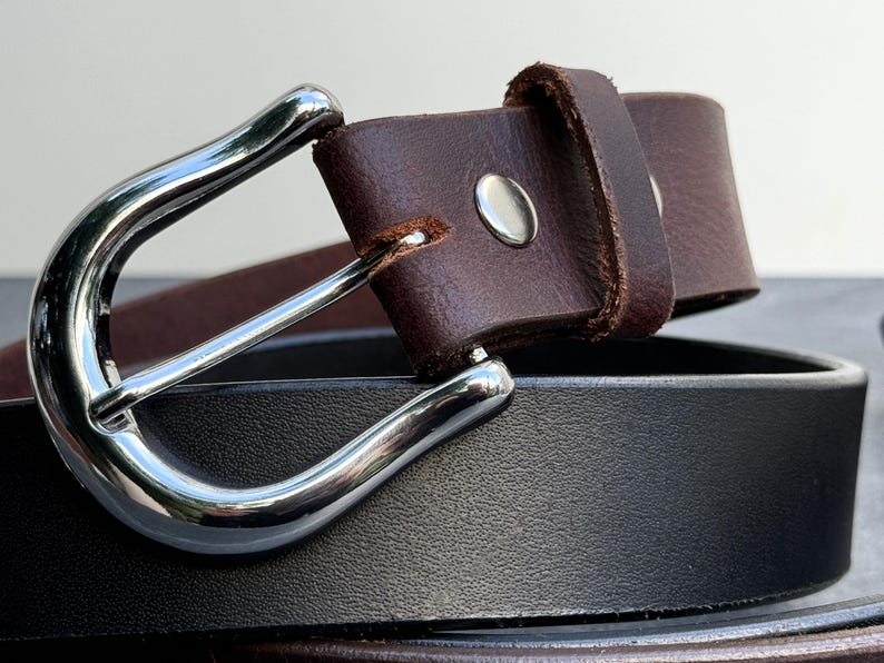 May include: A brown leather belt with a silver buckle. The belt is folded in half and the buckle is visible.