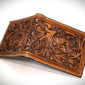 May include: A brown leather wallet with a tooled floral design. The wallet is closed and has a stitched edge.