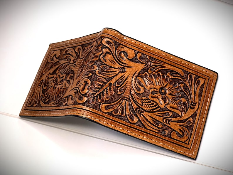 May include: A brown leather wallet with a tooled floral design. The wallet is closed and has a stitched edge.
