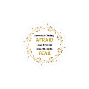 Può includere: Un adesivo dorato con una ghirlanda di foglie intorno al testo "Invece di avere PAURA, posso diventare qualcosa da TEMERE".