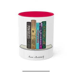 May include: White ceramic mug with a red rim. The mug features a graphic of a bookshelf with five books. The books are titled "The Inheritance Games", "Cinder", "Instant Karma", "Fourth Wing", and "Powerless". The text "Macie's Bookshelf" is printed below the graphic.