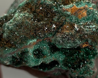 May include: A rough, green and brown rock with a crystalline texture. The rock is covered in small, green crystals.
