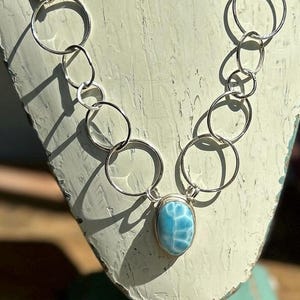 May include: A silver chain necklace with a large oval blue gemstone pendant. A matching blue gemstone bracelet and a smaller blue gemstone pendant are also pictured.