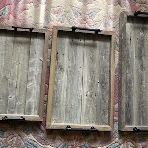 May include: A set of three rectangular wooden serving trays with black handles. The trays are made of weathered grey wood with a natural wood frame. The trays are different sizes, ideal for serving food or displaying items.