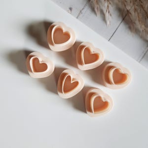 Op de afbeelding: Zes hartvormige koekjessnijders in een zachte perzikkleur. Elke snijder heeft een hartvormig binnendesign, waardoor een gelaagd effect ontstaat. De snijders zijn gerangschikt op een wit oppervlak, met een neutrale achtergrond.