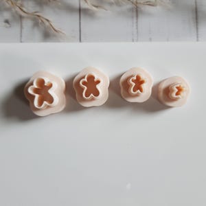 Könnte beinhalten: Vier hellpfirsichfarbene Ausstecher in Form von Lebkuchenmännern. Die Ausstecher sind in einer Reihe angeordnet, wobei die Größe von links nach rechts abnimmt. Die Ausstecher befinden sich auf einer weißen Oberfläche.