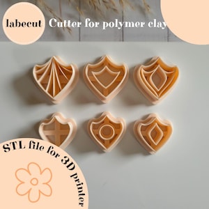 May include: Six beige polymer clay cutters in a shield shape with various interior designs. The cutters are arranged in two rows of three. The image includes the text "labecut Cutter for polymer clay" and "STL file for 3D printer".