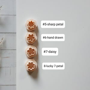 Pu&ograve; includere: Quattro formine per biscotti beige a forma di fiore con diversi disegni di petali. L'immagine include etichette di testo: "#5-sharp petal", "#6-hand drawn", "#7-daisy" e "8-lucky 7-petal". Ideali per la cottura e l'artigianato.