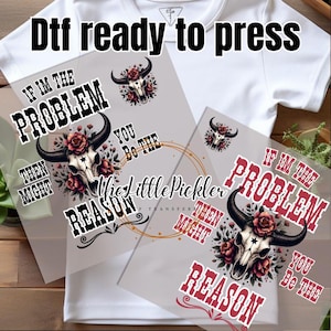 May include: White t-shirt with DTF (Direct to Film) transfers. The transfers feature a bull skull with roses and the text "If I'm the problem, then you might be the reason." The Little Pickler Transfer is also visible.