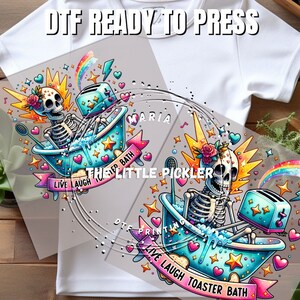 May include: A colorful digital transfer design featuring a skeleton in a bathtub with a toaster, hearts, stars, and the text "Live Laugh Toaster Bath".