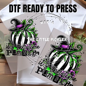 May include: DTF ready to press graphic featuring a black and white striped pumpkin wearing a witch hat with purple accents. The pumpkin has green slime dripping down its sides, with the text "it's Showtime Pumpkin". The Little Pickler.
