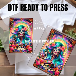May include: DTF ready-to-press transfer featuring a colorful illustration of a sugar skull makeup artist with turquoise hair, flowers, and makeup brushes. The design includes the text "THE MAKE UP ARTIST".