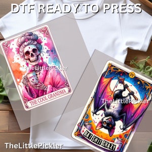 May include: Two iron-on transfers for t-shirts. One features a skeleton wearing a pink robe and holding a mug that says "SASSY". The text below reads "THE COOL GRANDMA". The other transfer features a bat with a colorful design and the text "BAT SHIT CRAZY".
