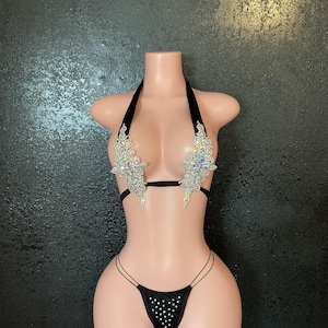 May include: Black bikini set with rhinestone embellishments. The halter top features sparkling crystal designs on the cups, and the matching bottoms have a string design with rhinestone accents. The set is displayed on a mannequin.