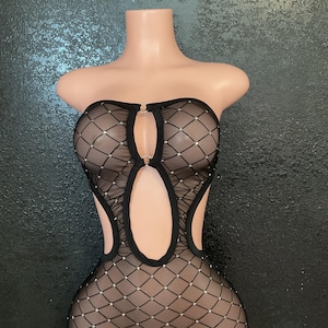 May include: Black fishnet dress with a strapless design, featuring a diamond pattern and small, sparkling embellishments. The dress has cut-out details and is displayed on a mannequin.