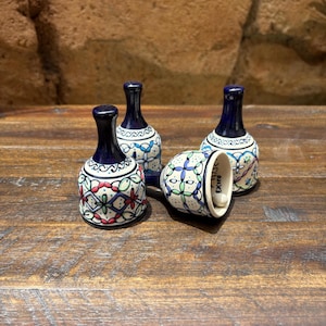 May include: Four small, decorative ceramic bells with a dark blue top and a white base. The bells are adorned with colorful floral patterns in red, green, and blue. One bell is lying on its side, revealing the interior.
