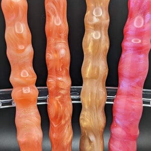 May include: Four colourful, swirled, acrylic pens in a clear plastic holder. The pens are in shades of orange, gold, and pink.