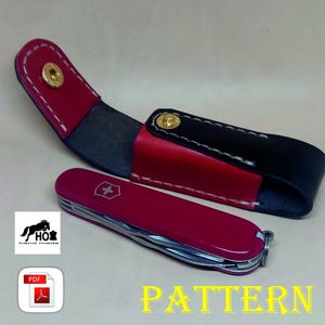 Puede incluir: Una funda de cuero roja con costuras blancas y una solapa de cuero negro. La funda está diseñada para guardar una navaja de bolsillo pequeña. La navaja es roja con una hoja plateada y una cruz blanca en el mango. El texto "PATTERN" está escrito en letras amarillas sobre un fondo blanco.