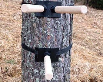 May include: Two wooden bars attached to a tree trunk with black metal brackets and straps. The bars are secured to the tree with black straps.