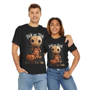 May include: Black t-shirts featuring a Halloween graphic. The graphic shows a scarecrow-like figure with a pumpkin head holding a jack-o'-lantern. The text "Trick or Treat" is above the figure. The shirts are worn by two people.