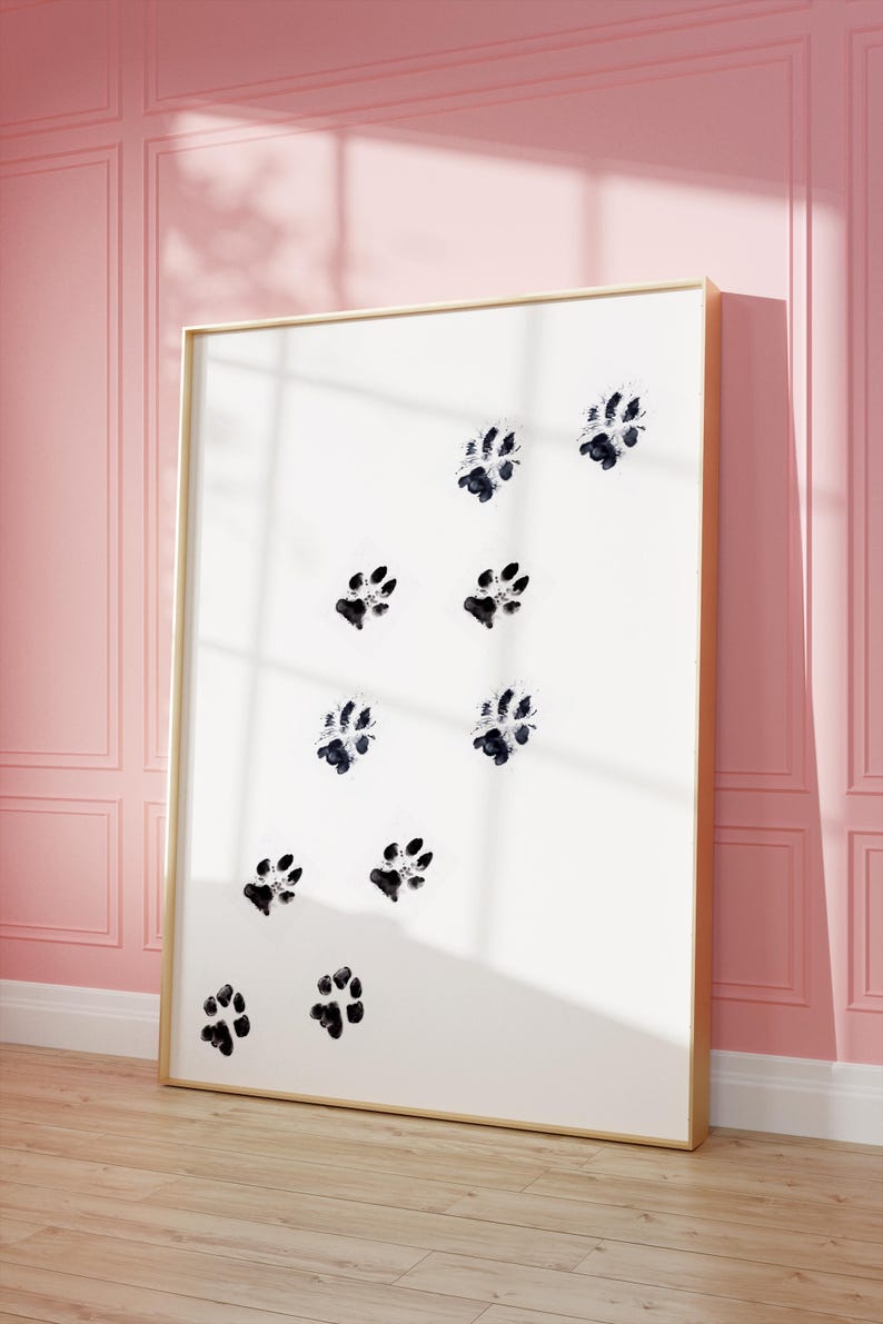 May include: A framed print with a white background and black paw prints in a scattered pattern. The frame is gold.