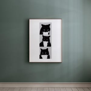 May include: A framed print featuring three black and white illustrations of a cat's face. The cat has a black body and a white bib. The artwork is displayed on a green wall.
