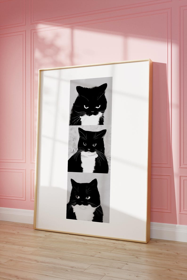 May include: Framed art print featuring three black and white cat portraits. Each cat has a black coat with white markings and a stern expression. The artwork is displayed in a gold frame against a pink wall.