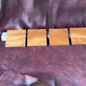 May include: Four square wooden coasters in a light brown color, arranged in a row on a brown leather surface.