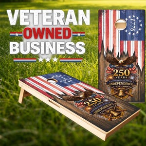 May include: A cornhole board set featuring a rustic American flag design with a bald eagle, a liberty bell, and text celebrating 250 years of United States independence from 1776 to 2026. The boards have a circular hole and a wooden frame structure.