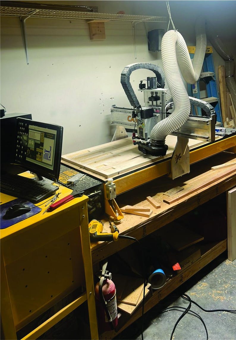 Puede incluir: Primer plano de una m&aacute;quina de fresado CNC con un panel de madera en la mesa. La m&aacute;quina est&aacute; conectada a un ordenador con un monitor que muestra un dise&ntilde;o. La fresadora est&aacute; en un taller con herramientas y restos de madera en el suelo.