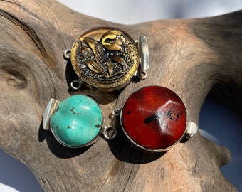 May include: Three silver and gemstone clasps for a bracelet or necklace. The clasps are round and feature a turquoise, red, and gold stone.