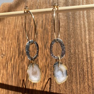 May include: A pair of gold hoop earrings with a textured silver oval charm and a white agate stone pendant.