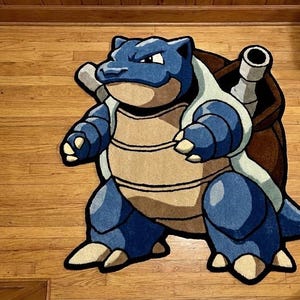 May include: A custom-shaped area rug featuring the character Blastoise from the Pokémon franchise. The rug displays the blue-skinned creature with a large brown shell, two prominent water cannons, and a tan-colored underbelly, outlined in black.