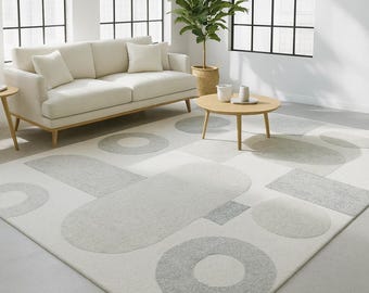 May include: A contemporary living room with a cream sofa, a round wooden coffee table, and a patterned rug. The rug features a white base with grey geometric shapes, including circles and rectangles. Large windows provide natural light.