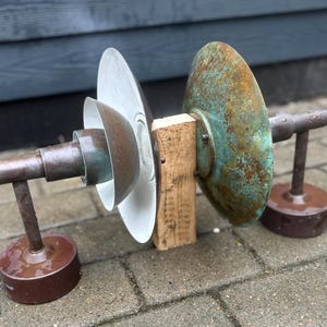 Puede incluir: Una escultura abstracta con componentes met&aacute;licos. La pieza incluye una varilla de color cobre con una base circular, que soporta una serie de elementos circulares y semicirculares. El elemento m&aacute;s grande tiene una p&aacute;tina verde.