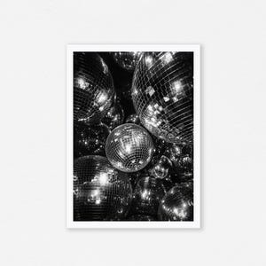 May include: A black and white photographic print featuring a cluster of multiple spherical disco balls. Each ball is covered in small, reflective square mirrors that catch and scatter light, creating a high-contrast pattern of bright highlights.