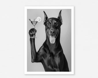 May include: Black and white photograph of a Doberman Pinscher holding a martini glass with a lemon slice. The dog is smiling with its tongue out. The image is set against a light gray background.