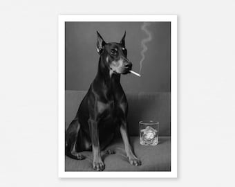 May include: Black and tan Doberman Pinscher sitting on a gray couch, smoking a cigarette. A glass of whiskey with ice sits to the right. The image is in black and white.