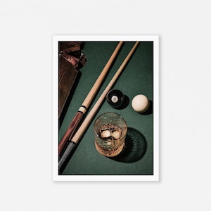 May include: A still life image featuring a green felt pool table with two cue sticks, a glass of whiskey with ice cubes, and billiard balls. The eight ball is black with a white number eight.